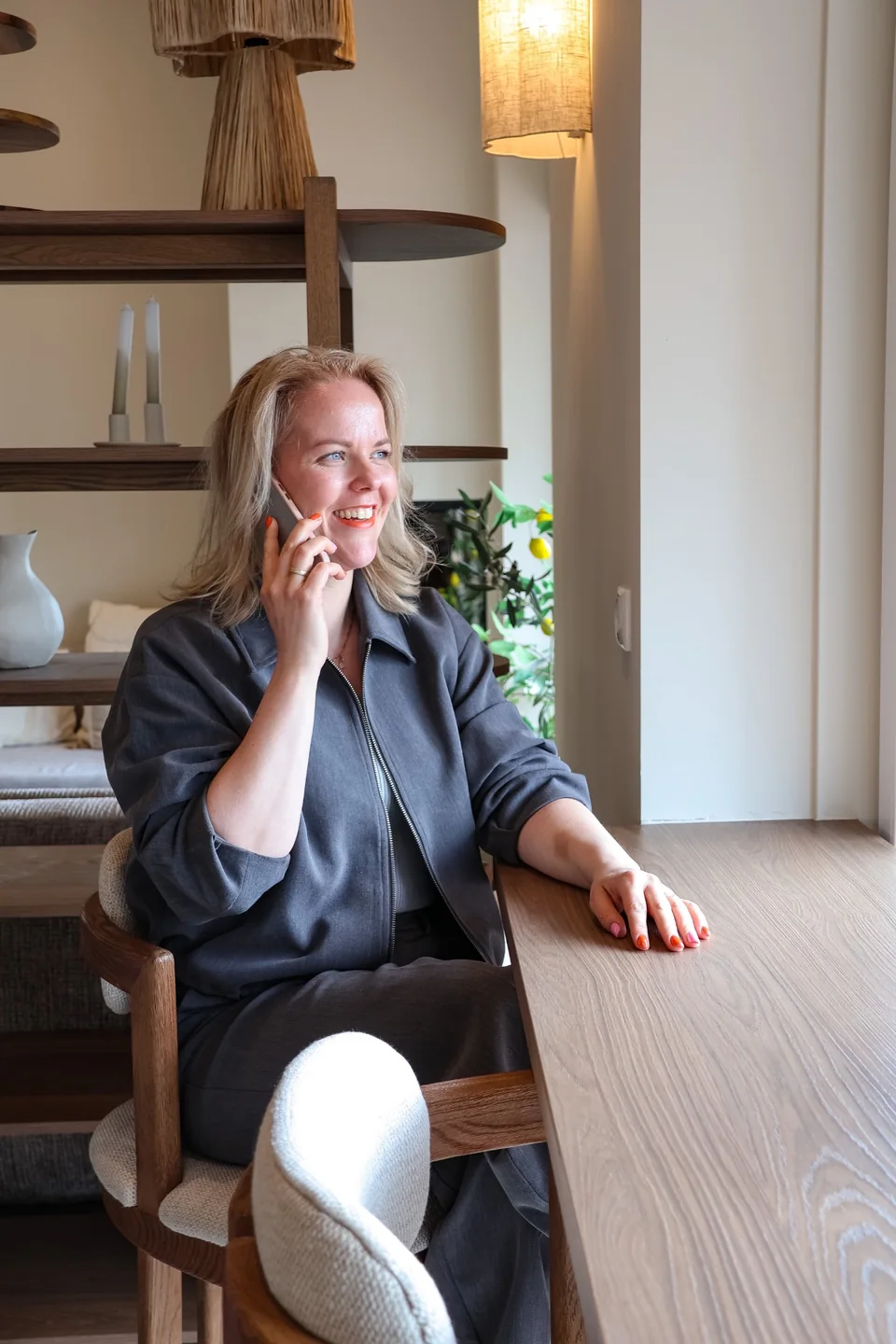 Anne lacht tijdens een telefoongesprek aan tafel bij het raam